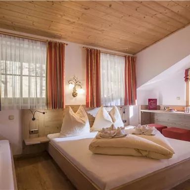 A cozy room with wooden floors and warm colors. It is well-lit and features large windows as well as a comfortable bed.