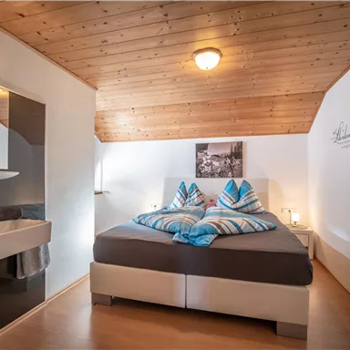 A cozy bedroom with a double bed and wooden ceiling. The room is modernly furnished and has an adjoining bathroom.