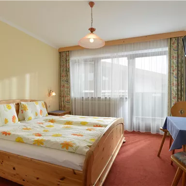 Ein gemütliches Schlafzimmer mit zwei Betten und bunten Blumenbettwäsche. Es gibt einen Tisch mit einem Pflanztopf und einen Fernseher an der Wand.