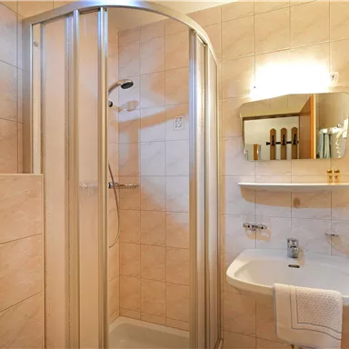 Ein modernes Badezimmer mit einer Duschkabine und hellen Fliesen. Auf dem Regal sind Pflegeprodukte und eine Pflanze sichtbar.