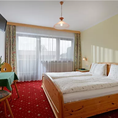Ein gemütliches Schlafzimmer mit zwei Betten und einem Tisch. Große Fenster sorgen für viel Tageslicht.