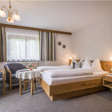 Ein komfortables Zimmer mit zwei Betten und einer gemütlichen Sitzecke. Große Fenster sorgen für viel Tageslicht.
