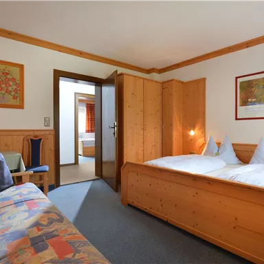 A cozy room with wooden furniture and a double bed. In the background, another room can be seen.