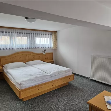 A bright bedroom with a double bed and wooden furniture. A television and a comfy armchair are also available.