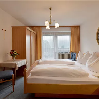 Ein gemütliches Schlafzimmer mit zwei Einzelbetten und hellen Vorhängen. Der Raum ist einladend und besitzt eine kleine Sitzecke mit Tisch und Stühlen.