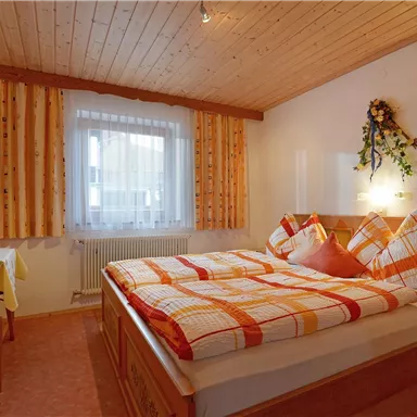 Ein gemütliches Schlafzimmer mit einem Doppelbett und orangefarbenen Kissen. Das Zimmer hat Holzvertäfelungen und ein Fenster mit viel natürlichem Licht.
