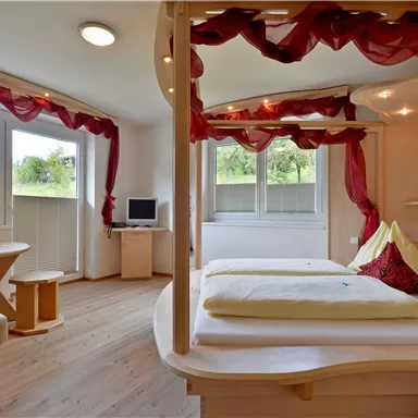 Ein helles Zimmer mit modernen Möbeln und großen Fenstern. Die Einrichtung ist gemütlich, mit einem Tisch und bunten Dekorationen.
