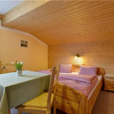 Ein gemütliches Schlafzimmer mit Holzdecke und zwei Betten. Neben den Betten steht ein Tisch mit Stühlen und einer Blumenvase.