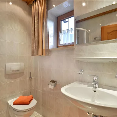A modern bathroom with a shower and a sink. There are bright tiles and orange towels.