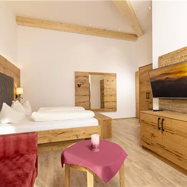 A modern room with wooden details and a cozy bed. The room features a television, a table, and a red couch.