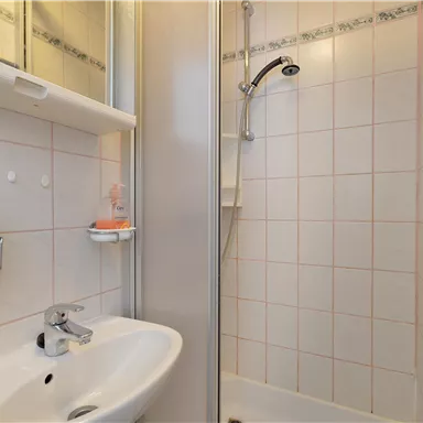 Ein kleines Badezimmer mit einer Dusche und einem Waschbecken. Die Wände sind gefliest und es gibt einen Spiegel an der Wand.