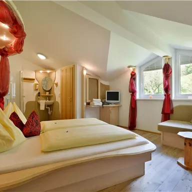 Ein gemütliches Zimmer mit einem modernen Design und großen Fenstern. Es gibt ein Doppelbett, eine Sitzecke und dekorative Vorhänge in Rot.