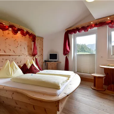 Ein gemütliches Zimmer mit Holzverkleidung und großen Fenstern. Es gibt ein Doppelbett, einen kleinen Tisch und einen roten Sessel.