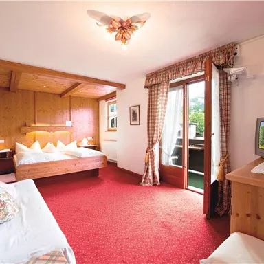 A cozy hotel room with wooden paneling and a large window. The room is bright and inviting, with a double bed and a television.