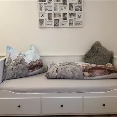 A cozy daybed with decorative cushions. A picture collage hangs on the wall.