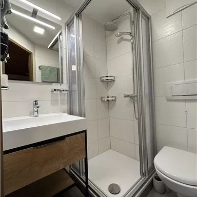 Ein modernes Badezimmer mit einer Duschkabine und einem Waschbecken. Die Wände sind hell gefliest und es gibt eine Toilettenschüssel.