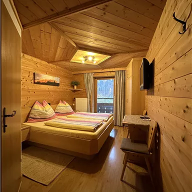 Ein gemütliches Holzzimmer mit zwei Betten und einem kleinen Tisch. Die Wände sind aus Holz und es gibt ein Fenster mit Blick nach draußen.