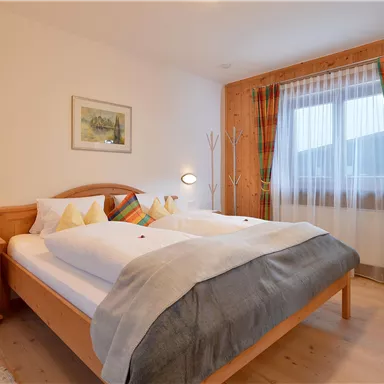 A cozy bedroom with a double bed and wooden furniture.  
Large windows with colorful curtains ensure plenty of light.