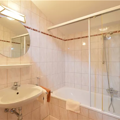 Ein helles Badezimmer mit einer Badewanne und einer Dusche. Der runde Spiegel und die geflieste Wand schaffen eine saubere und ordentliche Atmosphäre.