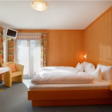 A cozy room with wooden paneling, a double bed, and two chairs. Large windows provide plenty of natural light.