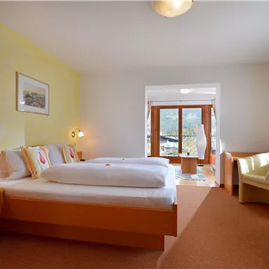 A bright room with two beds, warm colors, and large windows. There are cozy furniture and plenty of daylight.