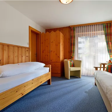 A cozy room with wooden furniture and carpet flooring. The windows are bright and let in a lot of light.