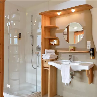 Ein modernes Badezimmer mit einer Dusche und einem Waschbecken. Holzregale und Handtücher verleihen dem Raum eine gemütliche Atmosphäre.