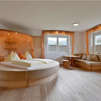 Ein gemütliches Zimmer mit runder Bettkonstruktion und hellem Holz. Die Fenster sind groß und sorgen für viel Licht, das angenehme Ambiente wird durch die sanften Vorhänge unterstrichen.