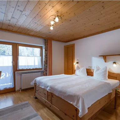 A cozy bedroom with a double bed and wooden paneling. Large windows let in plenty of daylight and offer a view outside.