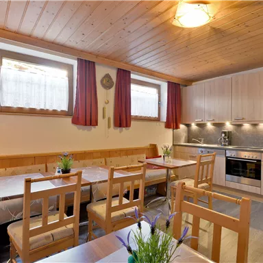 A cozy kitchen with wooden ceilings and bright furniture. There is a dining table with chairs and modern kitchen appliances.
