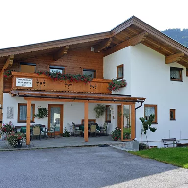 A beautiful wooden house with a balcony and a green area. Gentle hills can be seen in the background.