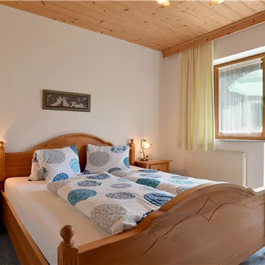 A cozy bedroom with a wooden bed and colorful bedding. There is a large window view of a balcony with a view.