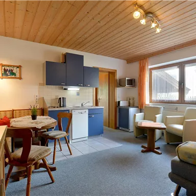 A cozy living room with a modern kitchen corner and a dining table. Large windows provide plenty of daylight and an inviting atmosphere.