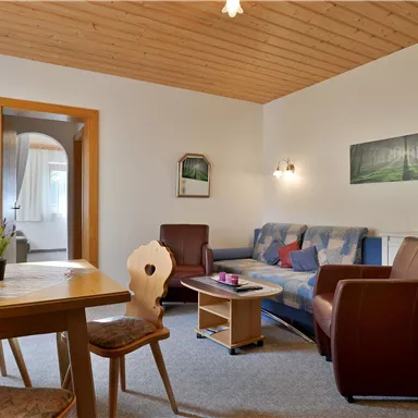 A cozy living room with a sofa and two armchairs. A table stands in the middle, and there is a door to another room.
