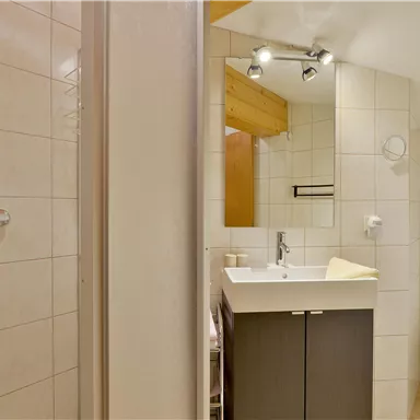 A modern bathroom with a shower, a sink, and a toilet. The walls are tiled, and the decor is bright and functional.
