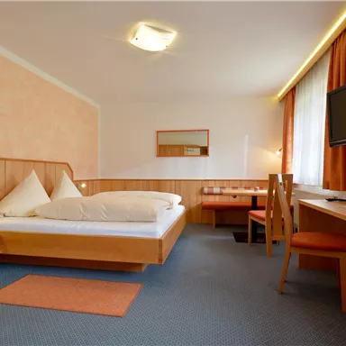 A cozy hotel room with a double bed and modern furniture. There is a desk, a television, and large windows that let in plenty of light.