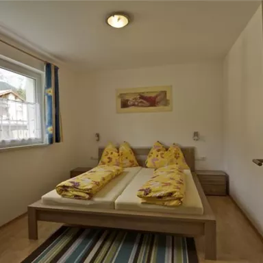 A simple bedroom with a double bed and yellow bedspreads. The room has a window with a view outside and a wooden floor.