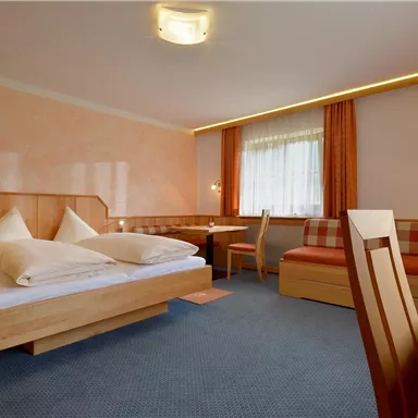 A cozy hotel room with two beds, a table, and a seating area. The walls are painted in soft colors, and the room feels bright and inviting.