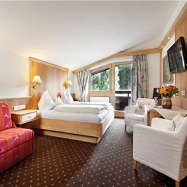 Ein gemütliches Hotelzimmer mit Holzverkleidung und einem großen Fenster. Es gibt ein Doppelbett, einen Fernseher und eine Sitzgruppe.