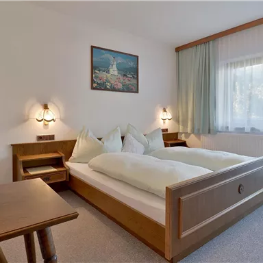 Ein helles Schlafzimmer mit zwei Betten und angenehmem Holzdekor. Neben dem Bett steht ein kleiner Tisch mit einer Blumenvase.