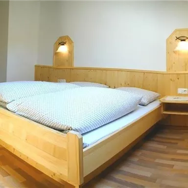 A cozy bedroom with a large wooden bed and bright walls. Next to the bed are two nightstands with lamps.