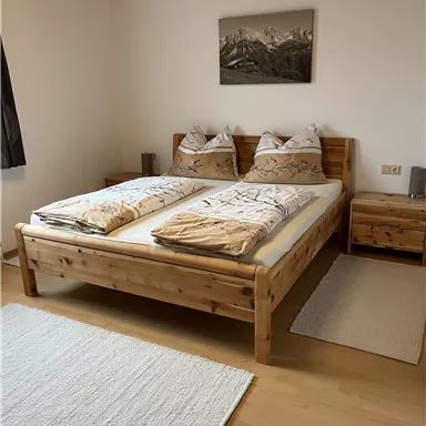 Ein gemütliches Schlafzimmer mit einem Holzbett und zwei Nachttischen. Die Wände sind hell und es gibt ein Bild mit Bergen an der Wand.