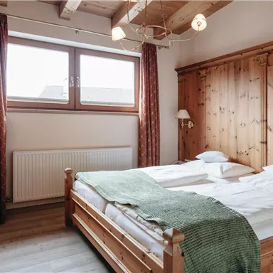 A cozy bedroom with a double bed and wood paneling. Large windows provide plenty of daylight and a warm atmosphere.