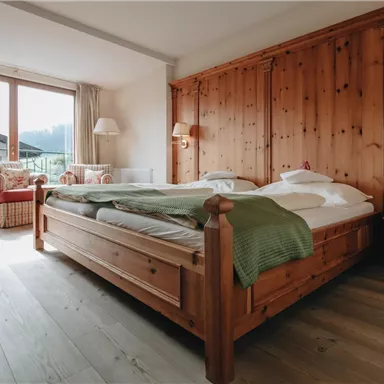 A cozy bedroom with a large wooden bed and soft textiles. There is a beautiful view of the mountains through the windows.