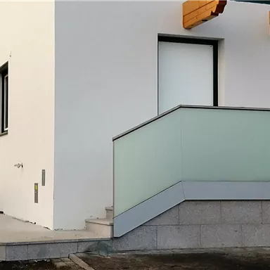 A modern building with a white facade and an entrance with a railing. The stairs lead to an entrance with large windows.
