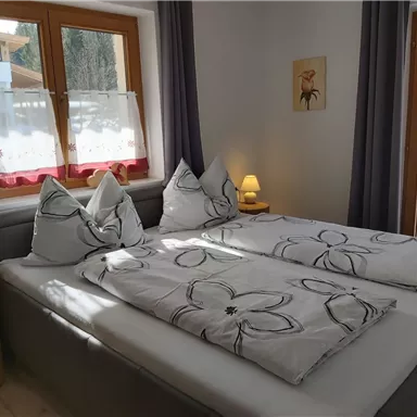A cozy bedroom with a double bed and modern cushions. The room has large windows that bring in plenty of daylight.