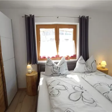 A cozy bedroom with two single beds and modern furniture. The windows are adorned with curtains, and there is soft lighting.