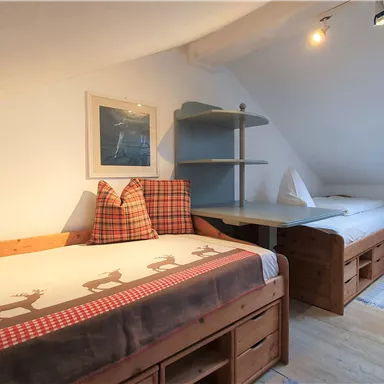 A cozy bedroom with two beds and a window. The walls are bright, and the furniture is made of wood.