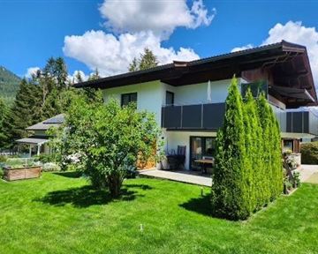 Ein modernes Haus mit einem schönen Garten und grünem Rasen. Es gibt Bäume und Sträucher im Freien, umgeben von einer malerischen Landschaft.