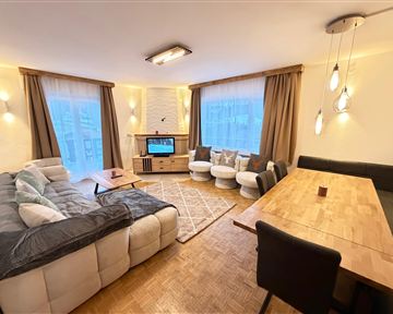 A modern living room with a comfortable couch, a table, and a television. Large windows provide plenty of natural light.